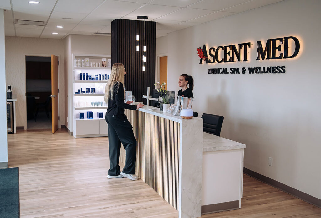 Patient standing and talking to woman at front desk in Ascent Med Spa
